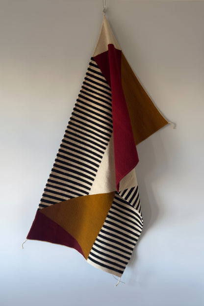 Handmade wool rugs with geometric pattern in black,, red, white and okra color  hanging on the wall
