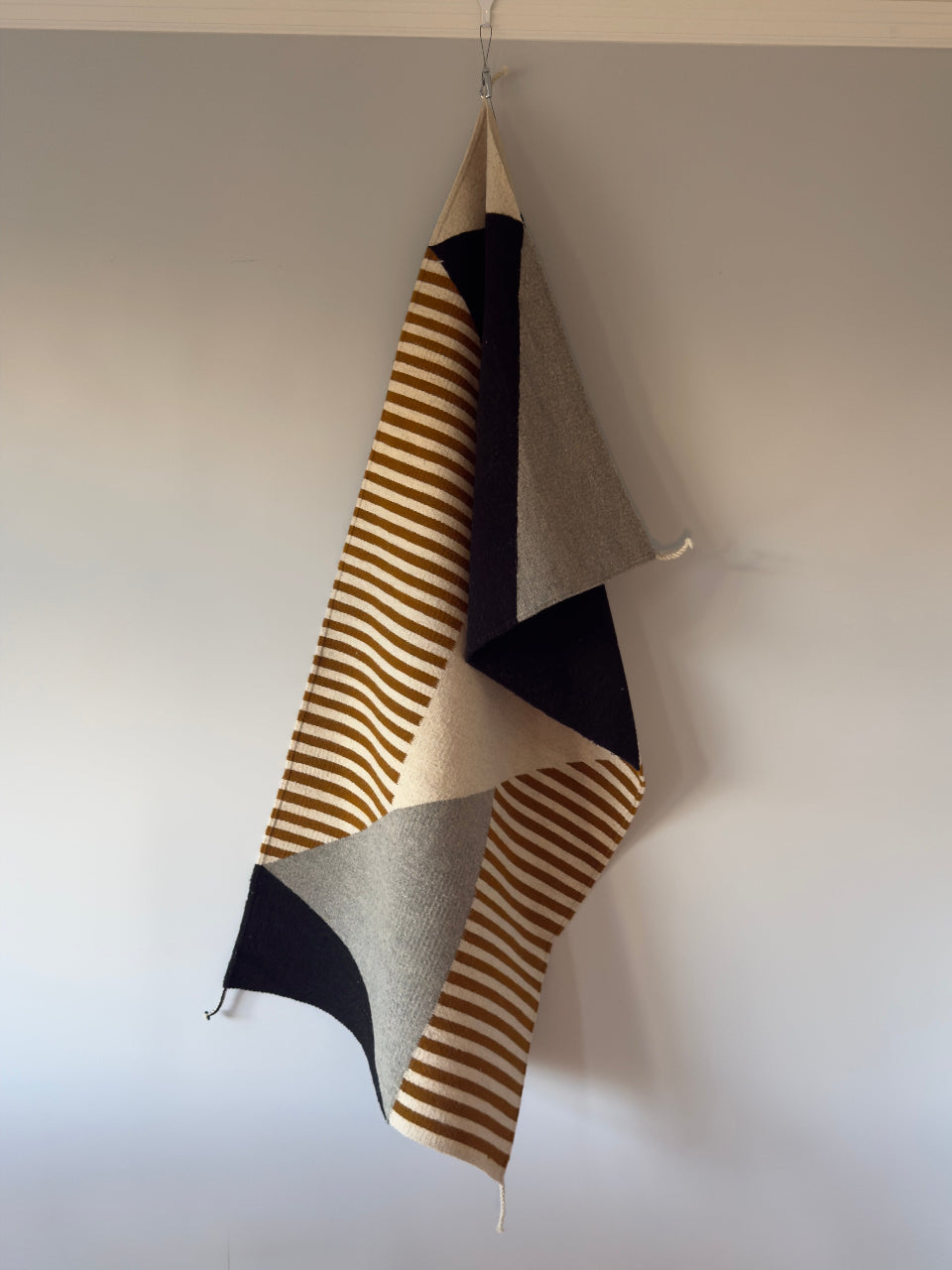 Handmade wool rug with geometric pattern in black, gray, white and okra color. Rug made in Oaxaca, Mexico by Zapotec weavers. Rug hanging 